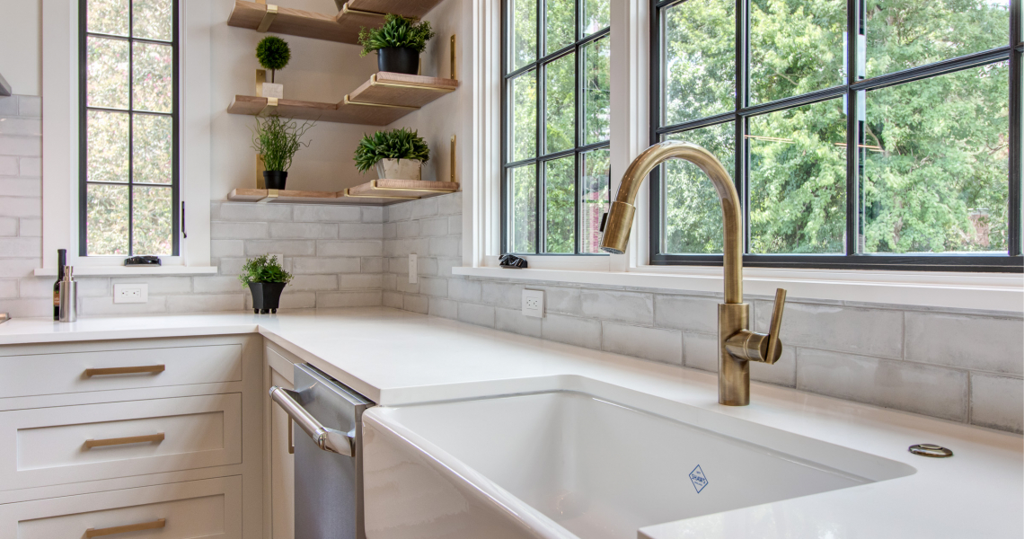 Farmhouse sink with antique brass faucet, open shelving, white counters, gold hardware.