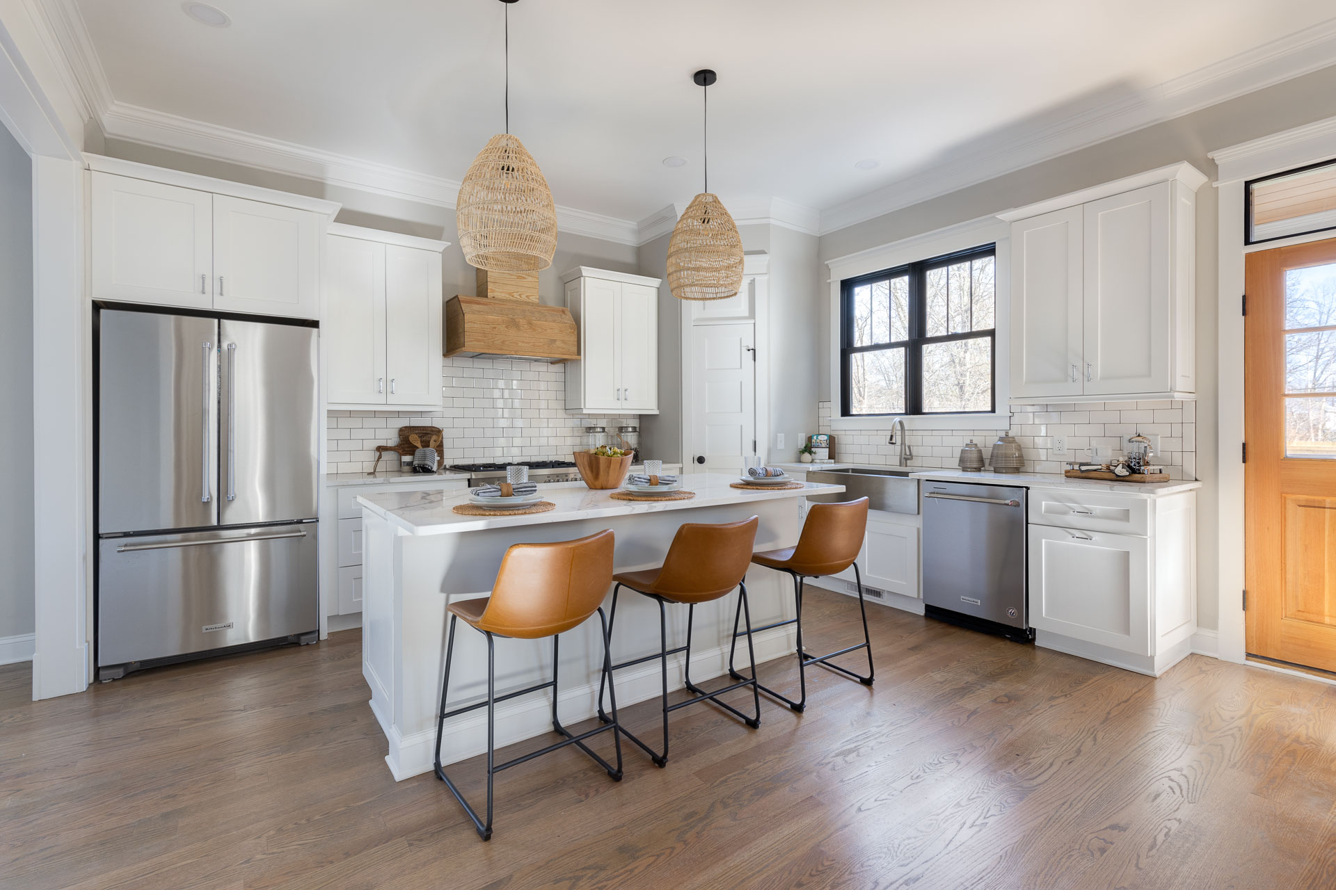 White kitchen with brown accents, with a white marble countertop island, stainless-steel appliances and a stainless steel vessel sink with matching kitchen faucet for listing photography in Durham, North Carolina.