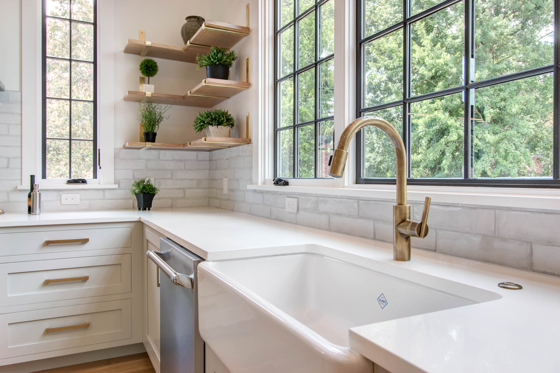 White vessel sink with gold faucet with white cabinets and gold hardware, stainless steel dishwasher and some small potted plants on some wooden shelves emphasizing interior designer photography in Durham, North Carolina.